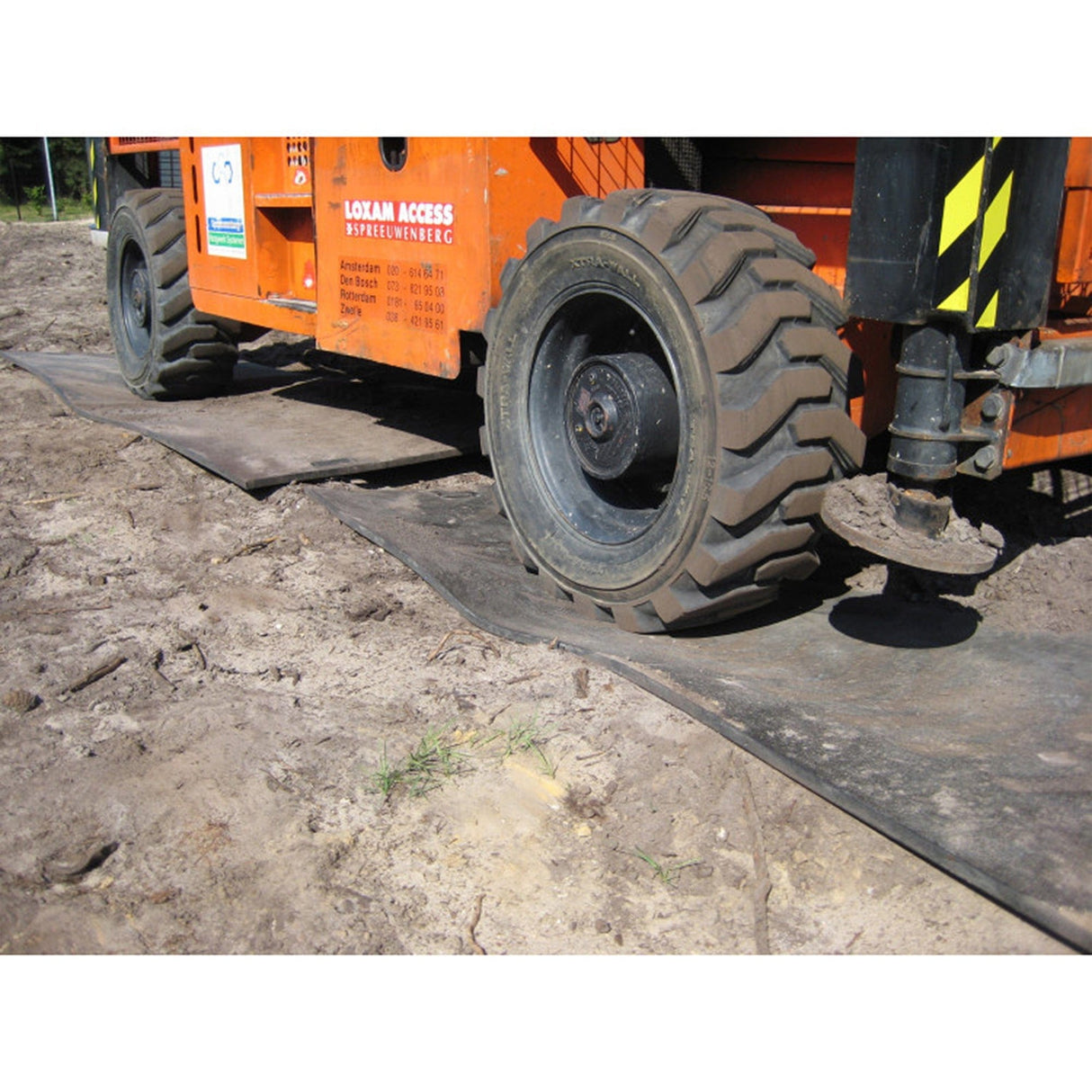 Wheeled access platform driving over EuroTrak access mats on bare ground