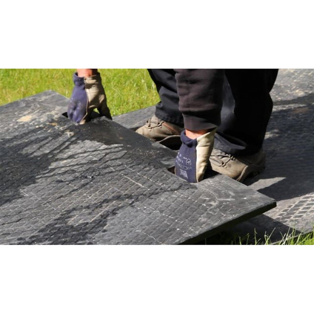 Workers in protective gloves lifting an EuroTrak access mat by its hand holes