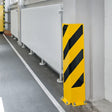 Right-angle protector bolted at a wall corner in an indoor corridor, guarding the edge next to pipework