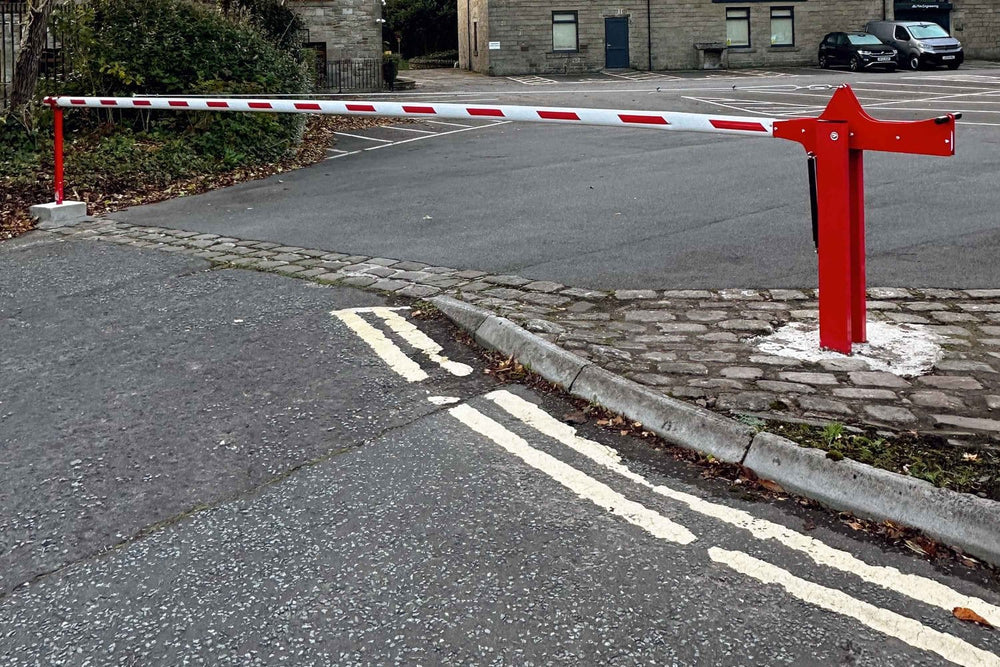 Red manual raise-arm barrier installed at a business car park entrance, with fresh concrete at the base of the post